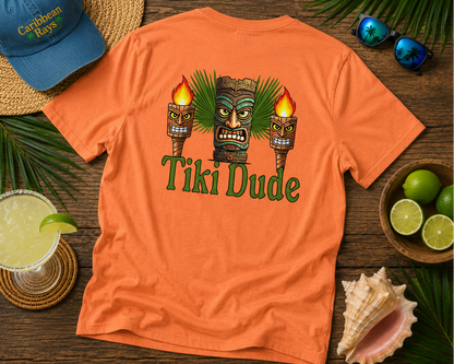 Orange t-shirt with 'Tiki Dude' design on a wooden surface with tropical accessories.