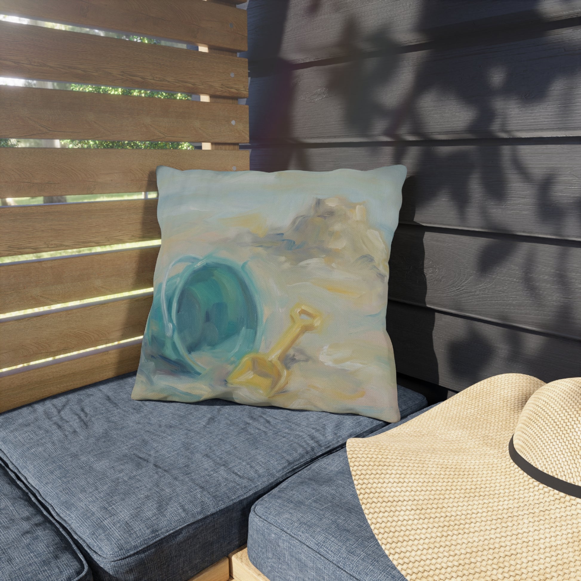 Decorative pillow with a sand bucket and shovel design on a cushioned bench.