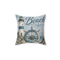 A square decorative throw pillow featuring a nautical design with a lighthouse, a large ship's wheel, rope, and the word 'Beach' in script on a light blue background.