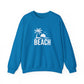 A bright blue crewneck sweatshirt with a white graphic on the chest depicting a palm tree, a rising sun, birds, and the word 'BEACH'.