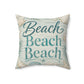 A square decorative throw pillow featuring the phrase 'Beach Beach Beach' in teal script and block lettering, surrounded by a seashell and palm leaf pattern on a light blue and beige background.