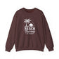 A heathered dark brown crewneck sweatshirt featuring a white graphic print of a palm tree, sunset, and the text 'BEACH Therapy IN SESSION' on the front, displayed against a solid white background.