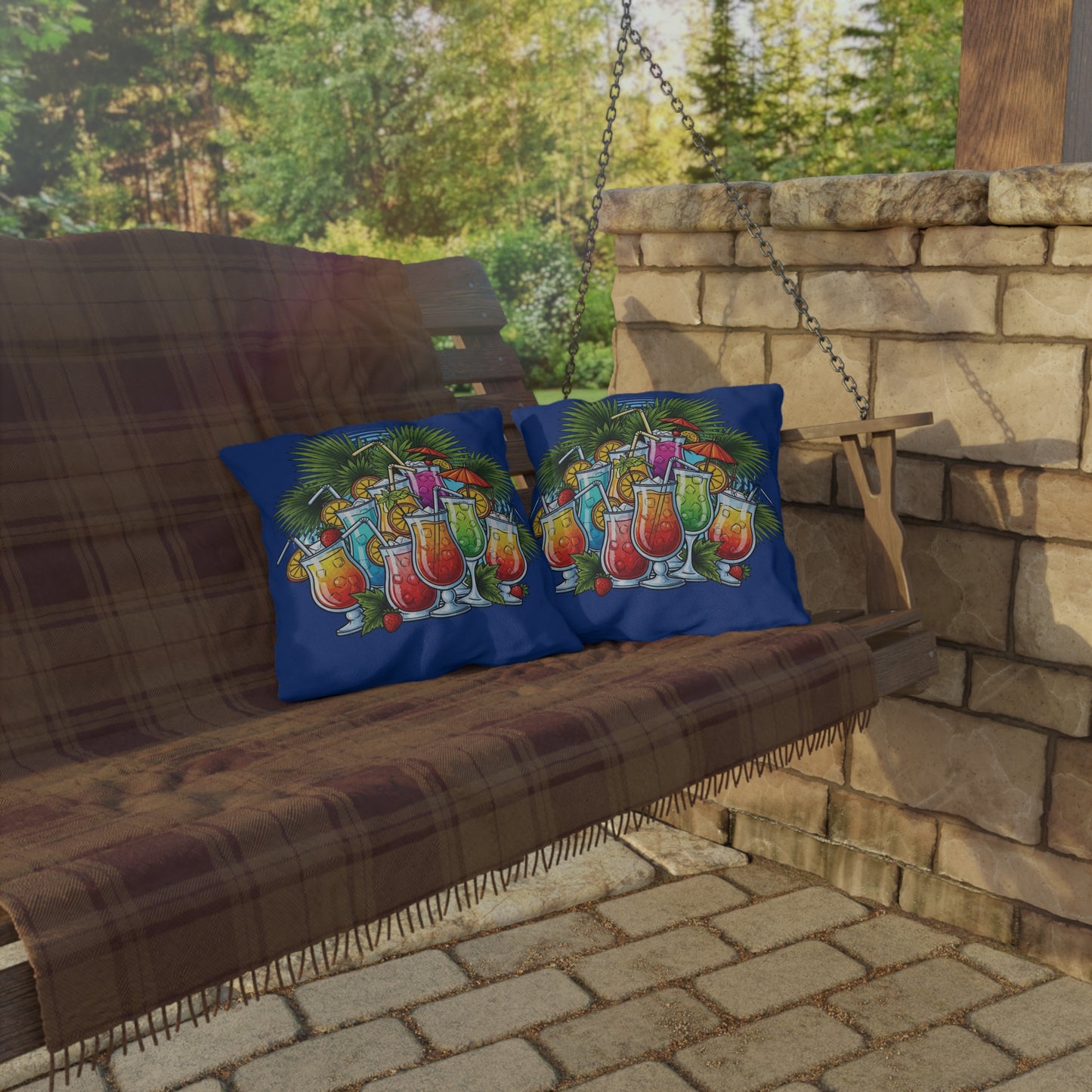 Two colorful pillows with tropical drink designs on a wooden swing bench outdoors.