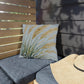 Gray outdoor cushions with a decorative pillow and a straw hat on a wooden bench.