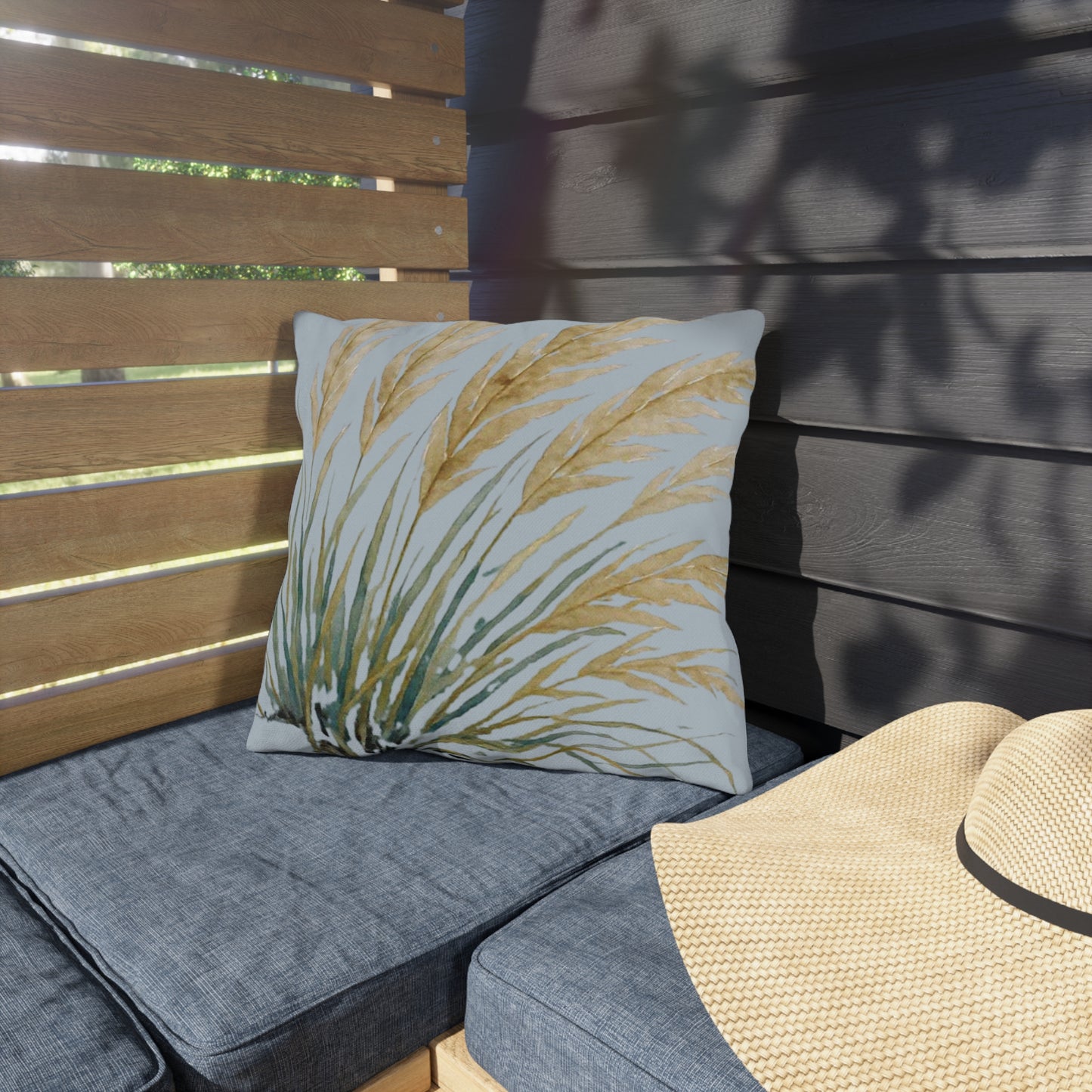 Gray outdoor cushions with a decorative pillow and a straw hat on a wooden bench.