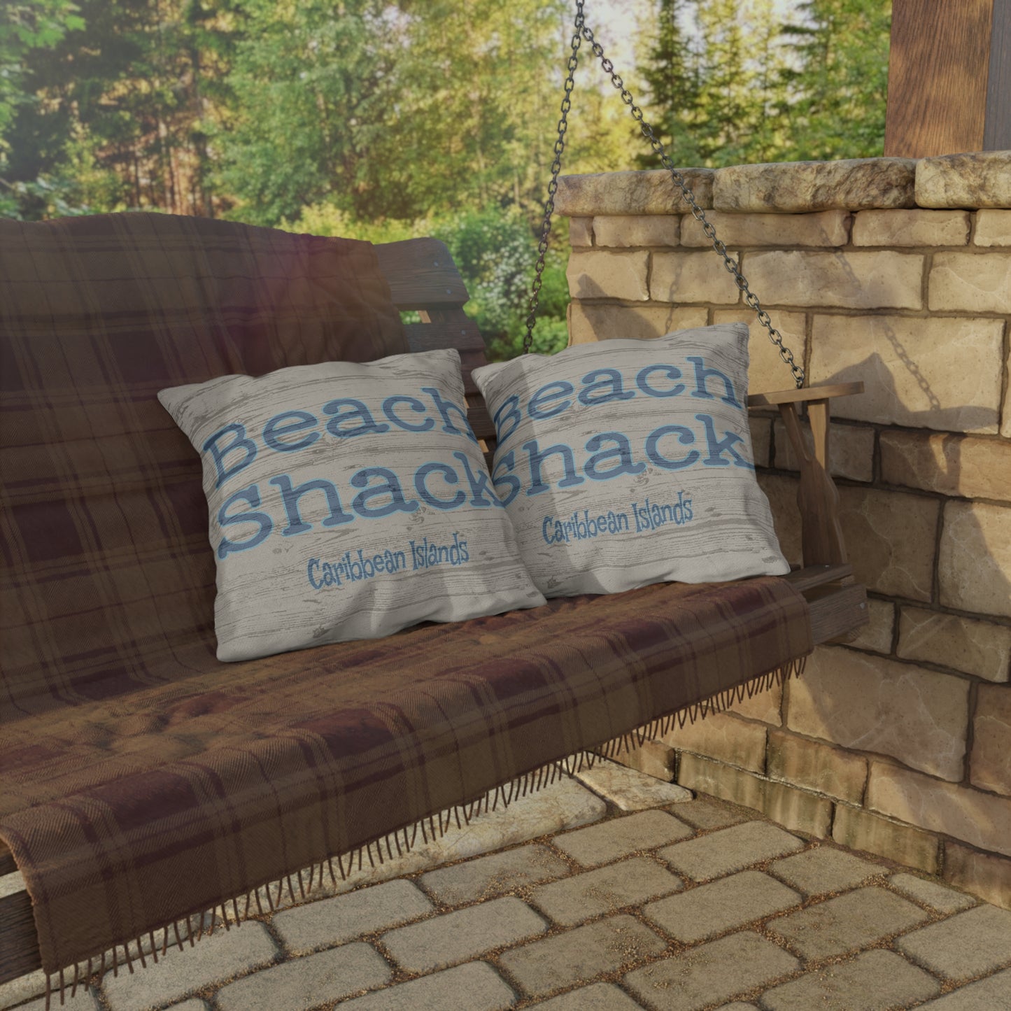 Wooden swing with 'Beach Shack' pillows against a stone wall and greenery.