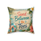 Square tropical beach pillow with “Sand Between the Toes” lettering and coral leaf accents