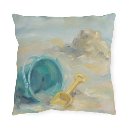 Decorative pillow with a beach scene featuring a blue bucket and yellow shovel.