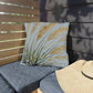 Decorative pillow with leaf pattern on a gray cushioned chair outdoors.