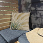 Outdoor seating with a decorative pillow and straw hat against a wooden wall.