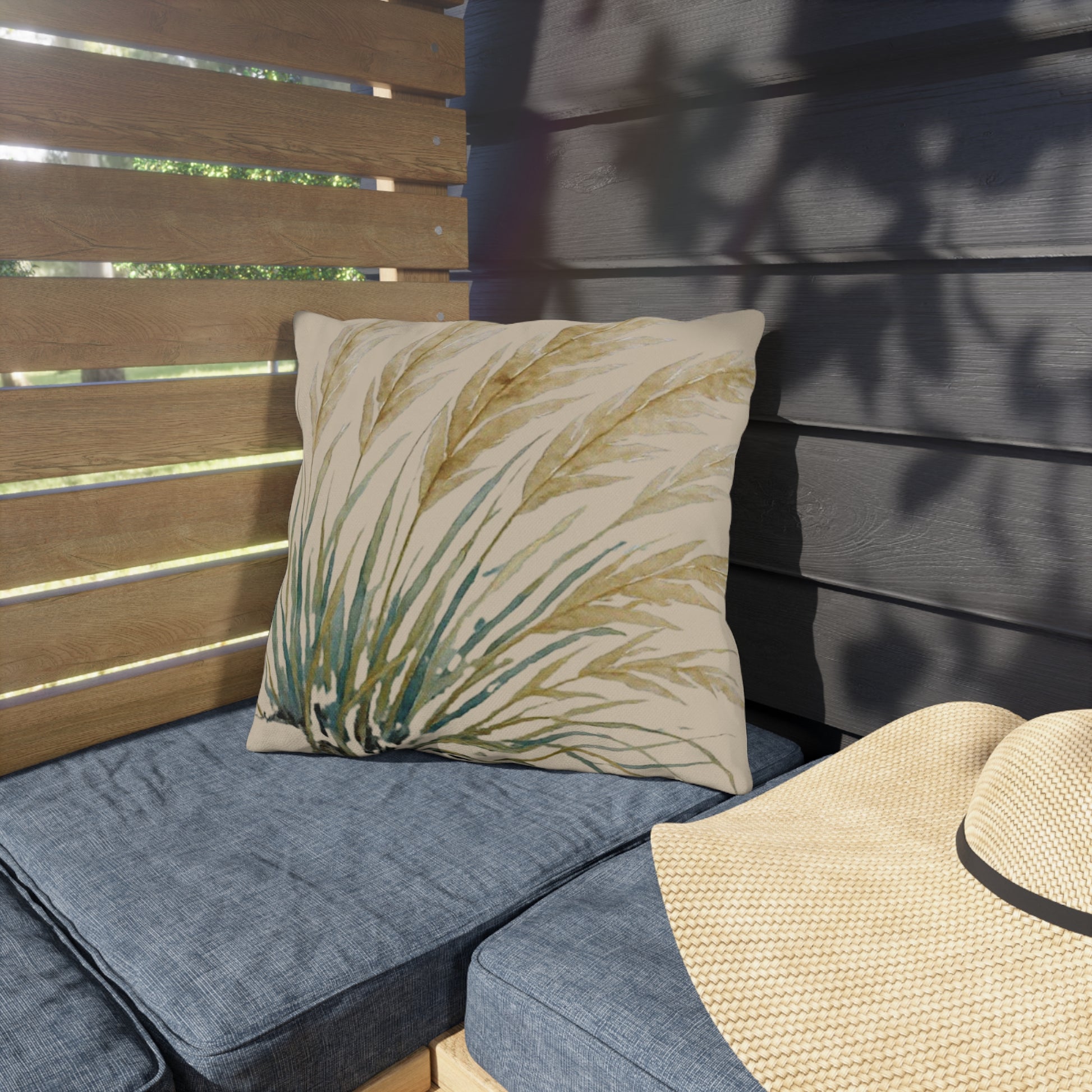 Outdoor seating with a decorative pillow and straw hat against a wooden wall.