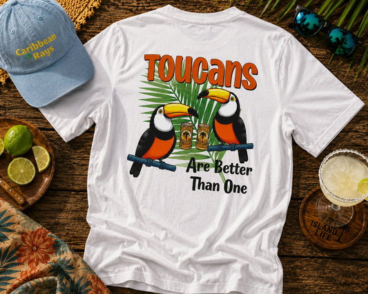 White t-shirt with toucan design and text on a wooden surface with a cap and drink.