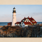 Lighthouse and buildings on a rocky coastline with a clear sky.