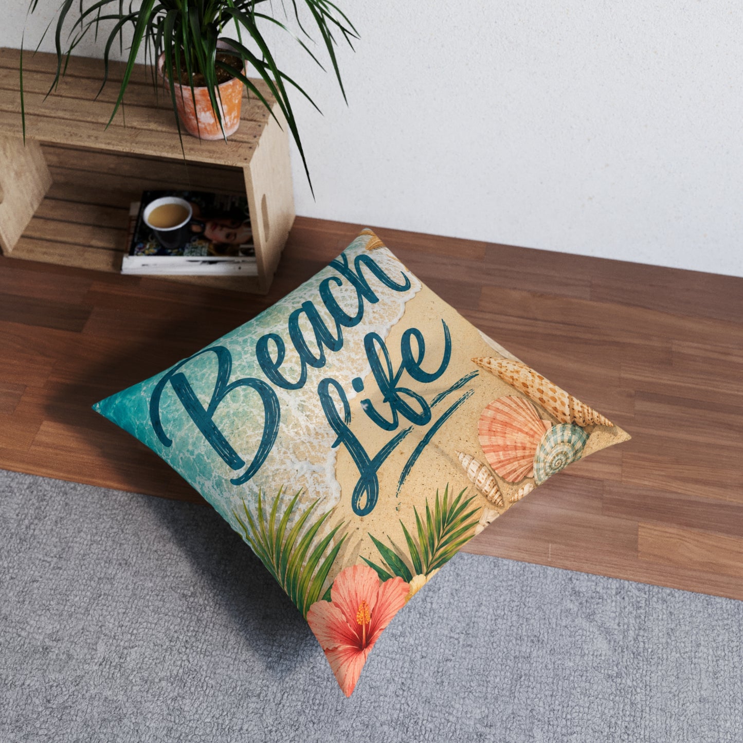 Square tufted floor pillow with 'Beach Life' seashell and palm print in beige and teal.