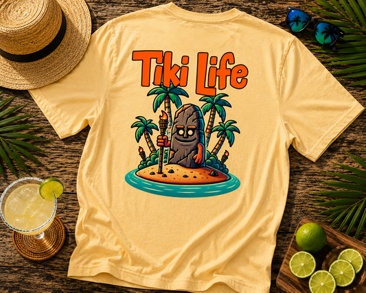 Beige t-shirt with 'Tiki Life' graphic design on a wooden surface with a hat, drink, and limes.