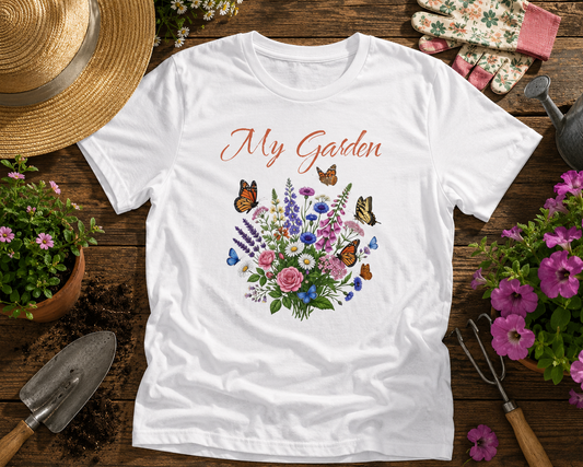 White t-shirt with floral design and 'My Garden' text on a wooden surface with gardening tools and plants.