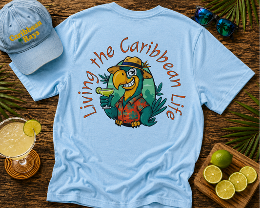 Light blue t-shirt with parrot graphic and 'Living the Caribbean Life' text, accompanied by a cap and tropical-themed items on a wooden surface.