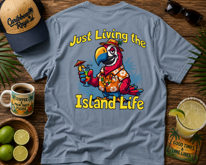 T-shirt with parrot graphic and 'Just Living the Island Life' text on a wooden surface with coffee, limes, and sunglasses.