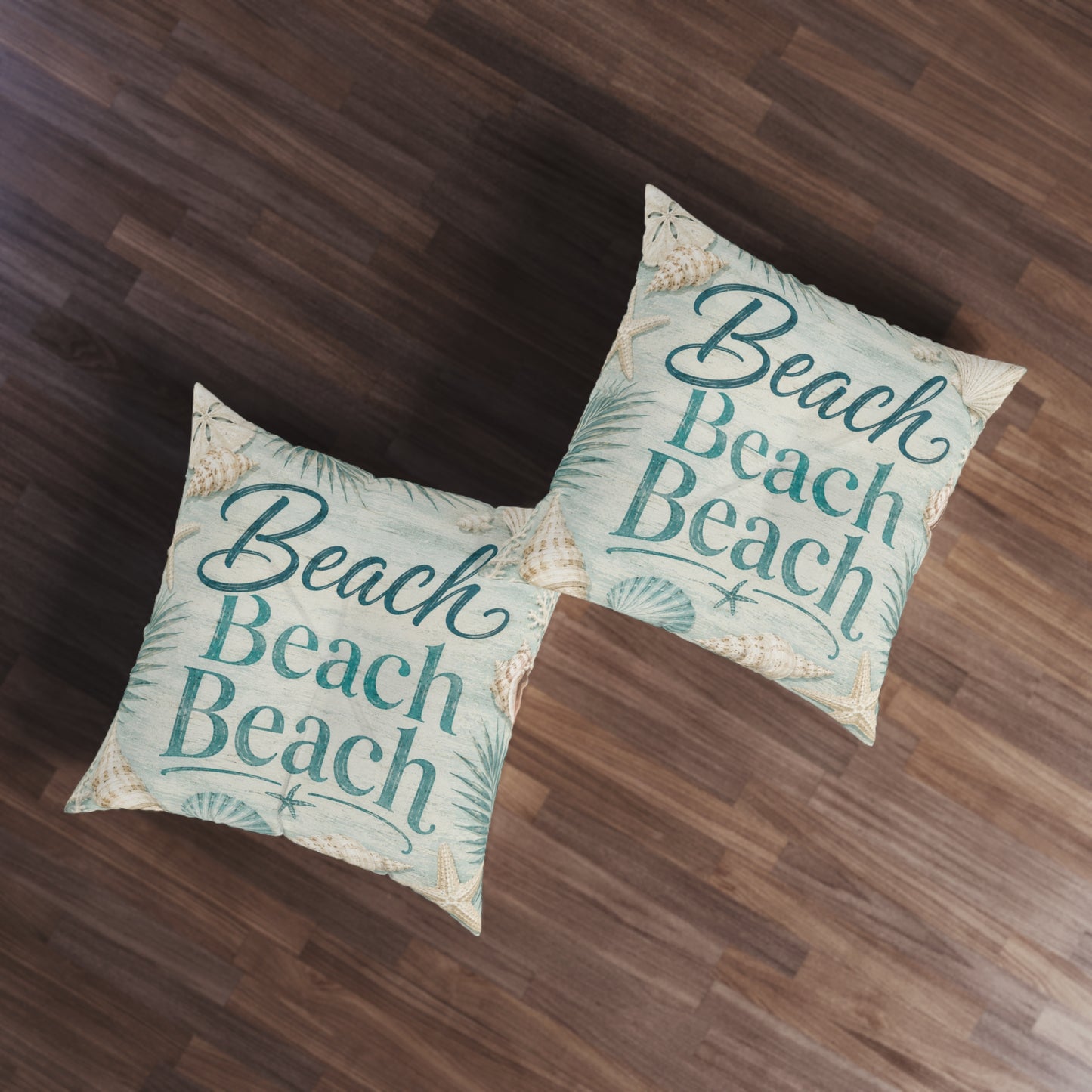 Square floor pillow set with teal “Beach Beach” print and seashell accents, two on wood floor