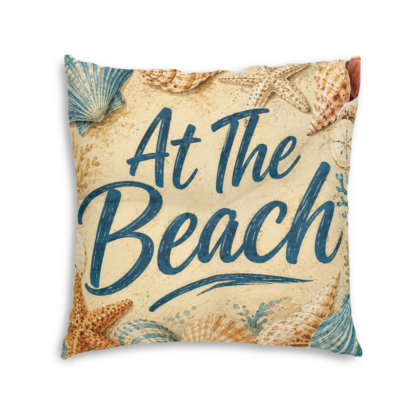 Square tufted floor pillow close-up, beige with seashells and teal 'At The Beach' lettering