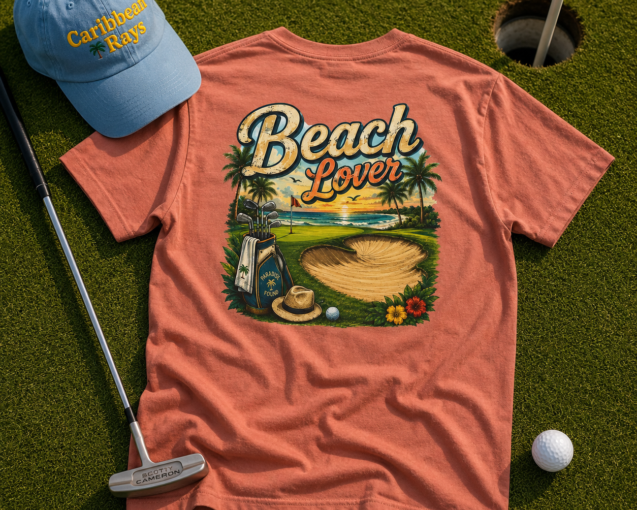 Beach Lover t-shirt with a golf-themed design on grass next to a blue cap and golf club.