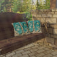 Porch swing with flip-flop patterned pillows against a stone wall and greenery.