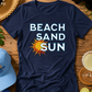 Navy blue t-shirt with 'Beach Sand Sun' design on a wooden surface with beach accessories.