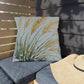 Decorative pillow with leaf pattern on a gray cushioned chair outdoors.