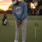 a man putting  wearing Blue crewneck sweatshirt featuring a circular graphic on the chest with the words 'PUTT FOR DOUGH' and an illustration of a golf putt.