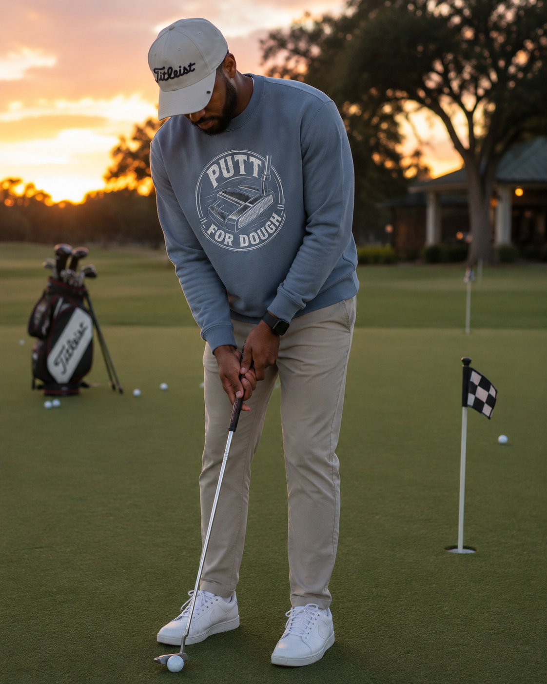 a man putting  wearing Blue crewneck sweatshirt featuring a circular graphic on the chest with the words 'PUTT FOR DOUGH' and an illustration of a golf putt.