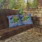 Two pillows with a parrot design and text on a wooden swing against a stone wall and greenery background.