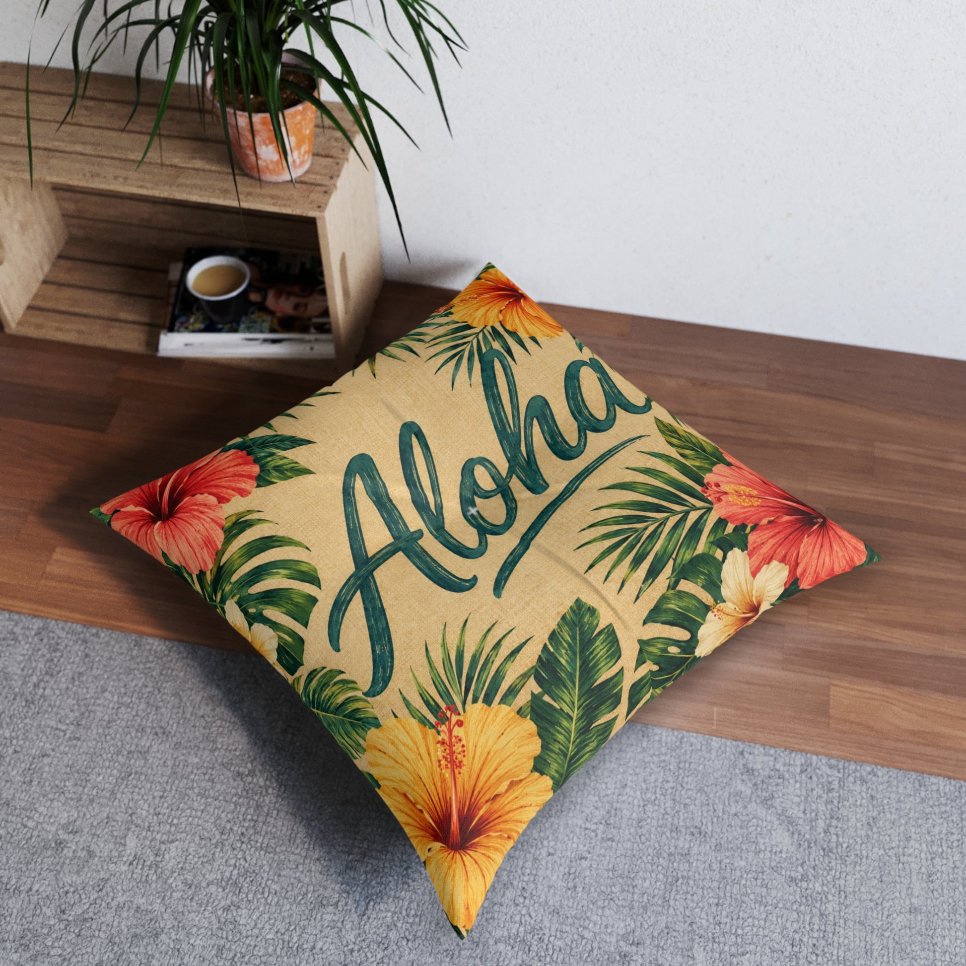 Square tufted floor pillow featuring teal Aloha script with hibiscus flowers and palm leaves on tan