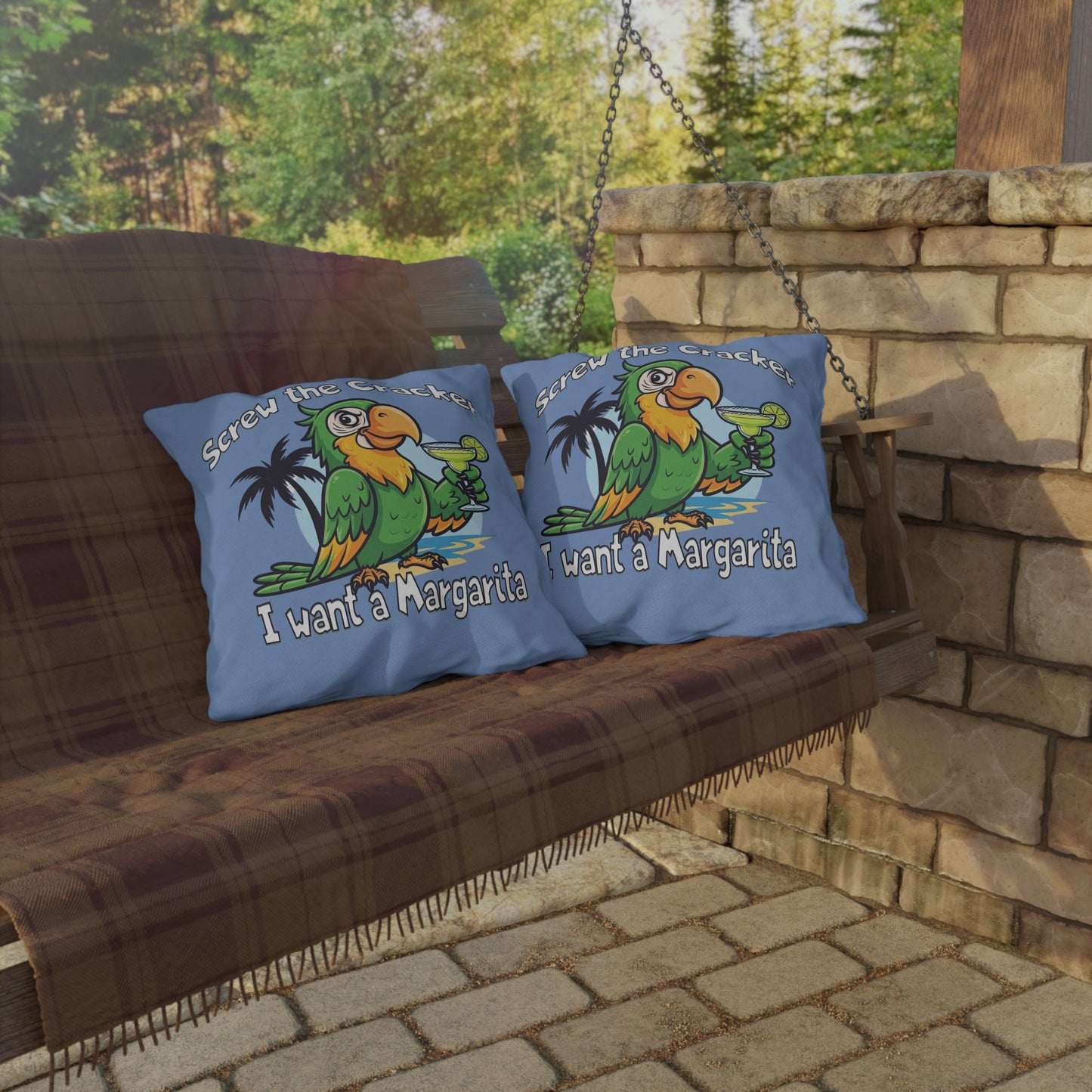 Two pillows with parrot graphics and text on a wooden swing against a stone wall and greenery background.