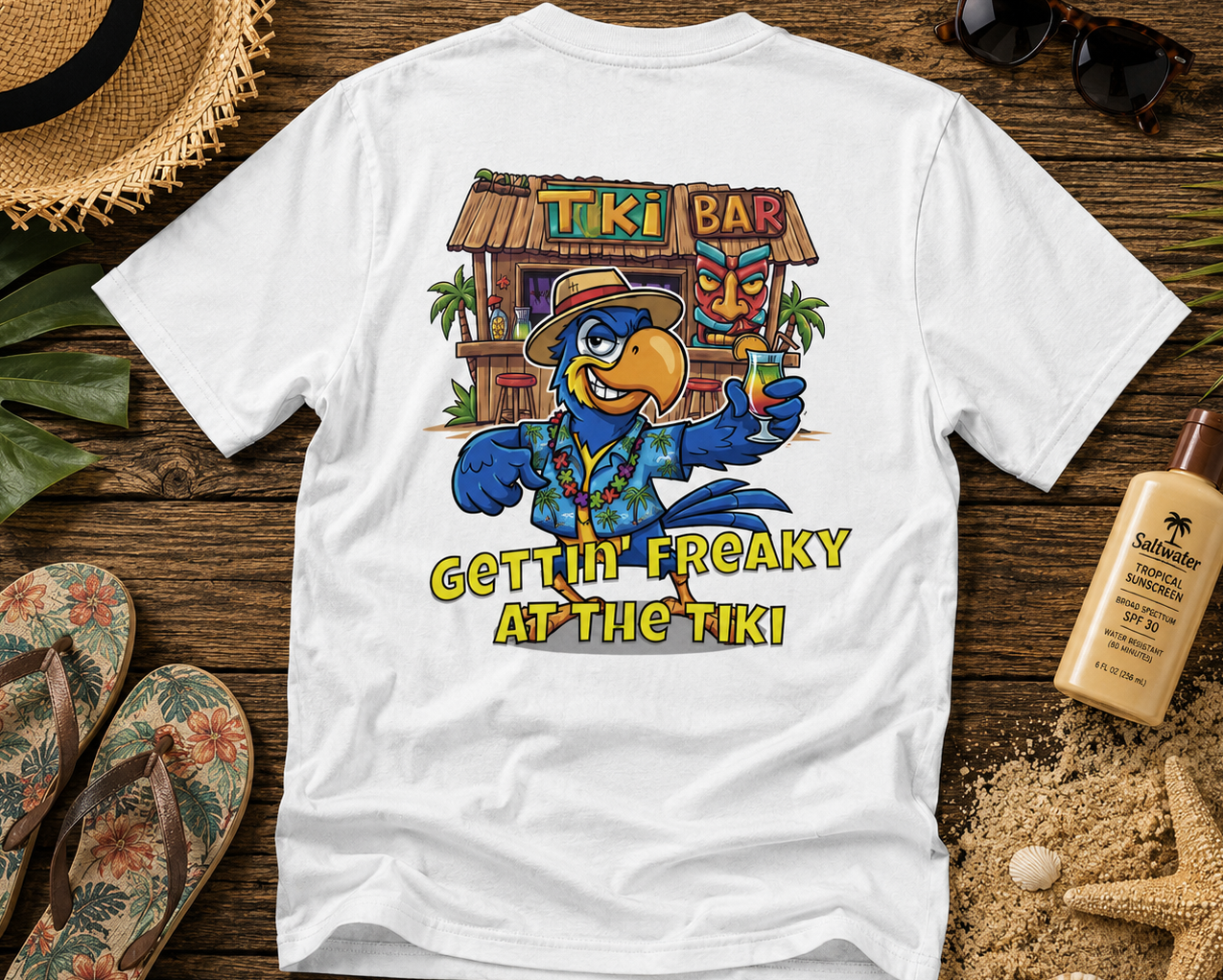 White t-shirt with a colorful tiki bar design and text on a wooden surface with beach accessories.