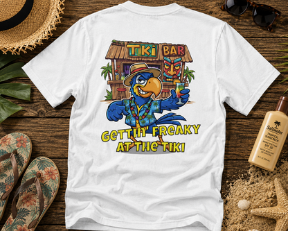 White t-shirt with a colorful tiki bar design and text on a wooden surface with beach accessories.