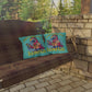 Two pillows with 'Island Life' design on a wooden swing against a stone wall and greenery background.