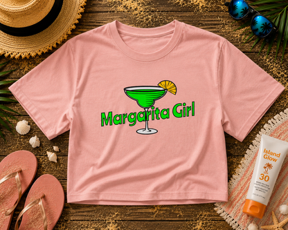Pink t-shirt with 'Margarita Girl' design on a wooden surface with summer accessories.