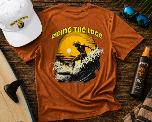 Orange t-shirt with a graphic of a surfer and 'Riding the Edge' text, white cap, sunglasses, and sunscreen on a wooden surface.