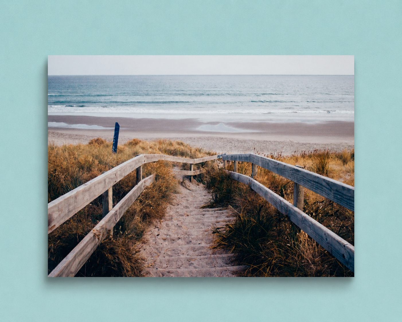 Wooden pathway leading to a beach with grass and ocean view on a light blue background