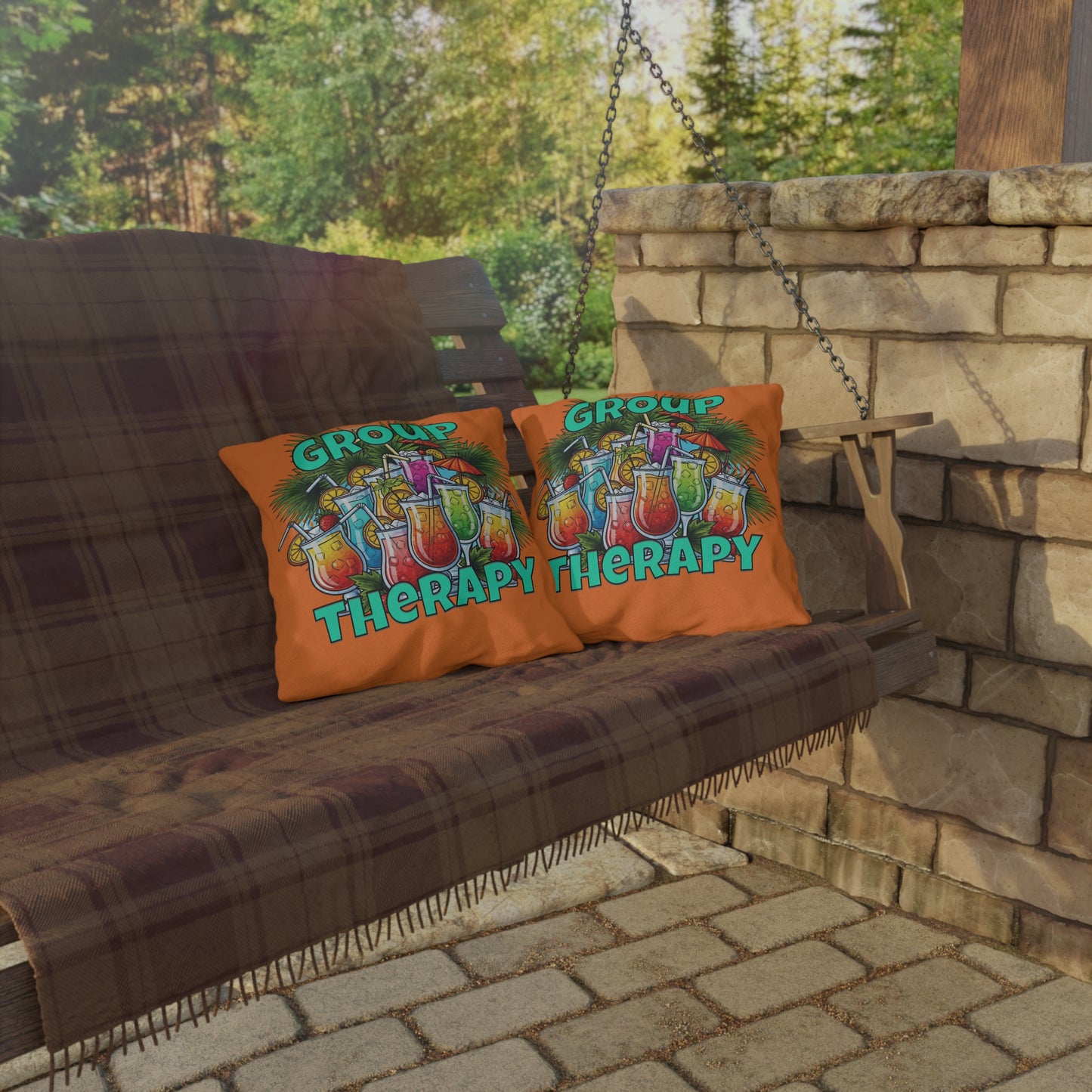Two pillows with 'Group Therapy' text on a wooden swing against a stone wall and greenery background.
