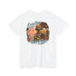 A white short-sleeve crewneck t-shirt featuring a colorful graphic print on the front. The graphic depicts a hula dancer wearing a lei and sunglasses, surrounded by tropical flowers, a guitar, and the text 'Every Hour at the Tikie Bar is Happy Hour'.