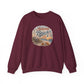 A maroon crewneck sweatshirt with a circular graphic on the chest that reads 'Autumn Beach Life' in stylized lettering over a beach scene illustration, shown against a plain white background.