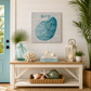 Nautical-themed decor with a shell painting, lantern, and books on a wooden bench.