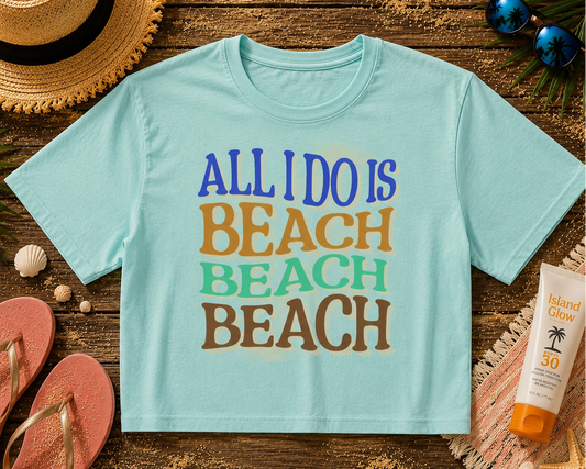 Light blue t-shirt with 'All I Do is Beach' text on a wooden surface with beach accessories.