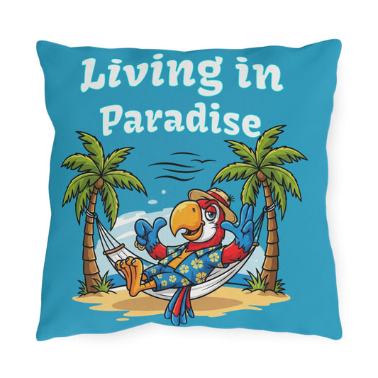 Pillow with a parrot in a hammock between palm trees and 'Living in Paradise' text on a blue background