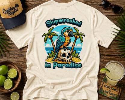 White t-shirt with a colorful parrot graphic and text 'Shipwrecked in Paradise' on a wooden surface with limes and a hat.