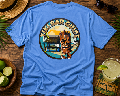 Blue t-shirt with a Tiki Bar Guide graphic on a wooden table with a hat, limes, and a drink.