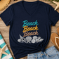 A navy blue V-neck t-shirt with a 'Beach Beach Beach' graphic in teal, yellow, and orange, styled in a flat lay with denim shorts, flip-flops, a straw hat, sunglasses, and starfish on a wooden surface.
