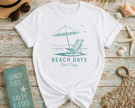 White t-shirt with 'Beach Days Best Days' design on a wooden surface with beach-themed accessories.