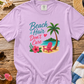 Purple t-shirt with beach-themed design on a wooden surface with beach accessories.
